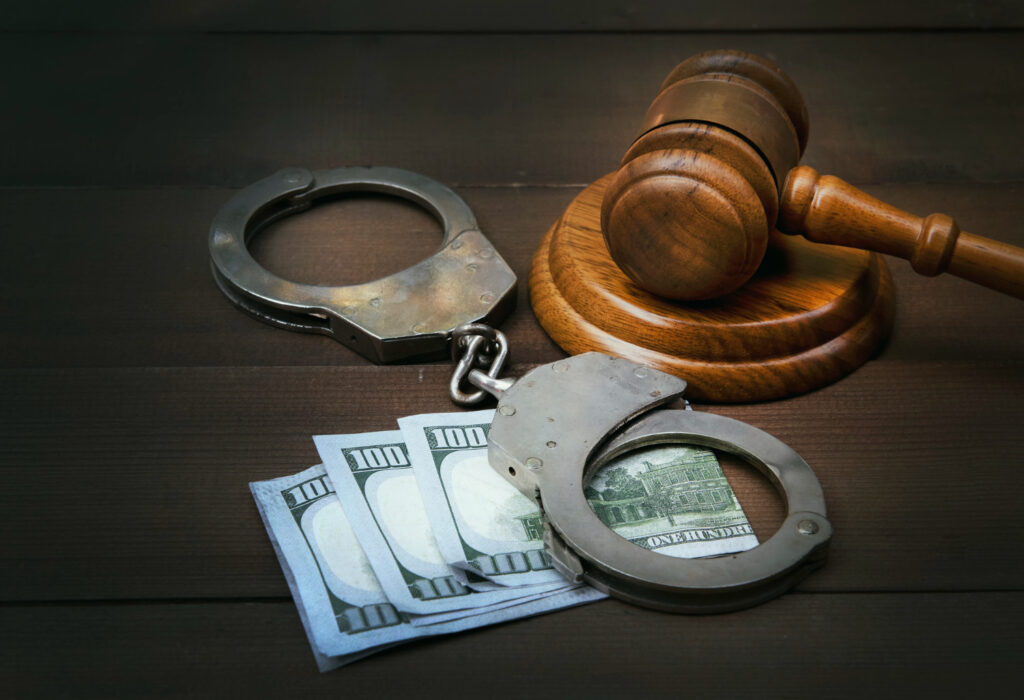 Handcuffs, cash, and a judge's gavel on a wooden surface, symbolizing legal consequences of financial crime or bribery.